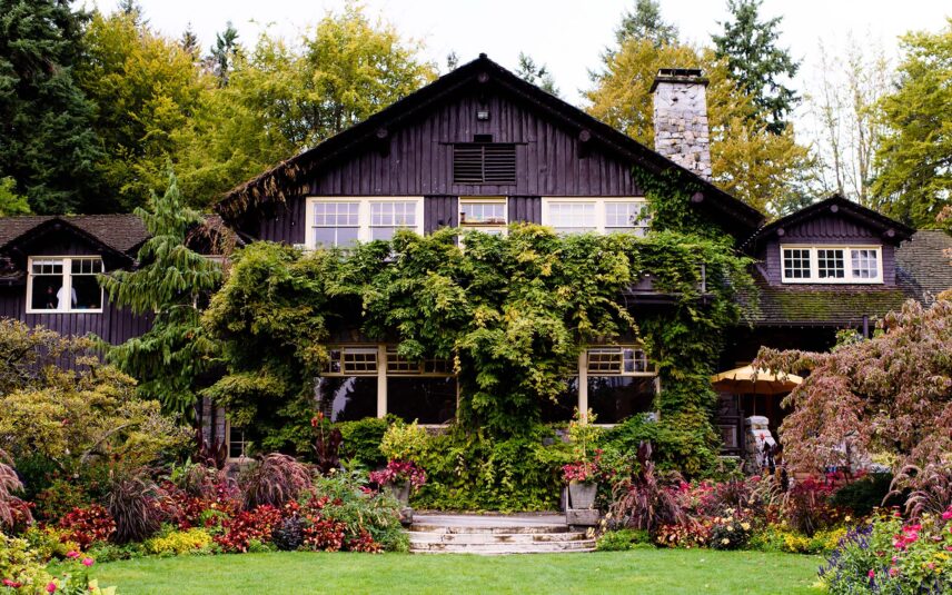 Front view of the Stanley Park Pavilion, a heritage-style building with white trim, dark wooden beams, and a sloping roof, surrounded by trees and gardens in Vancouver’s Stanley Park