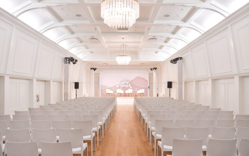 The Stanley Park Pavilion is set up for a corporate speaking event, chairs are set up in clean white lines towards the stage.