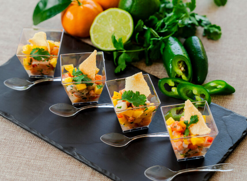 Little, clear bowls hold a mixture of vegetables, with accompanying spoons, as an appetizer.