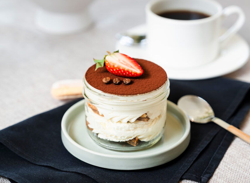 A dessert with a strawberry on top, and coffee beans, sits beside a black coffee.