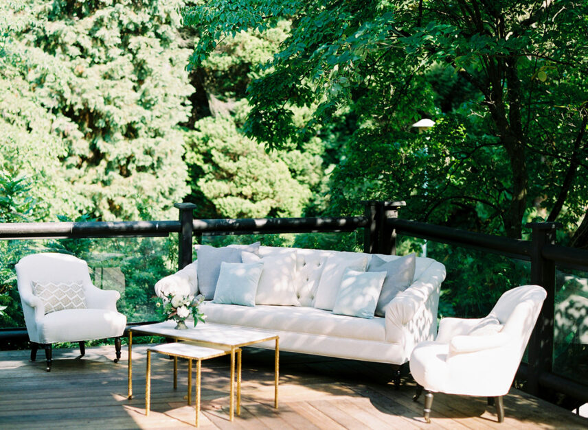 Outside seating set up for a specific event at Stanley's Bar and Grill. White sofas and armchairs are set up amongst tables holding flower arrangements