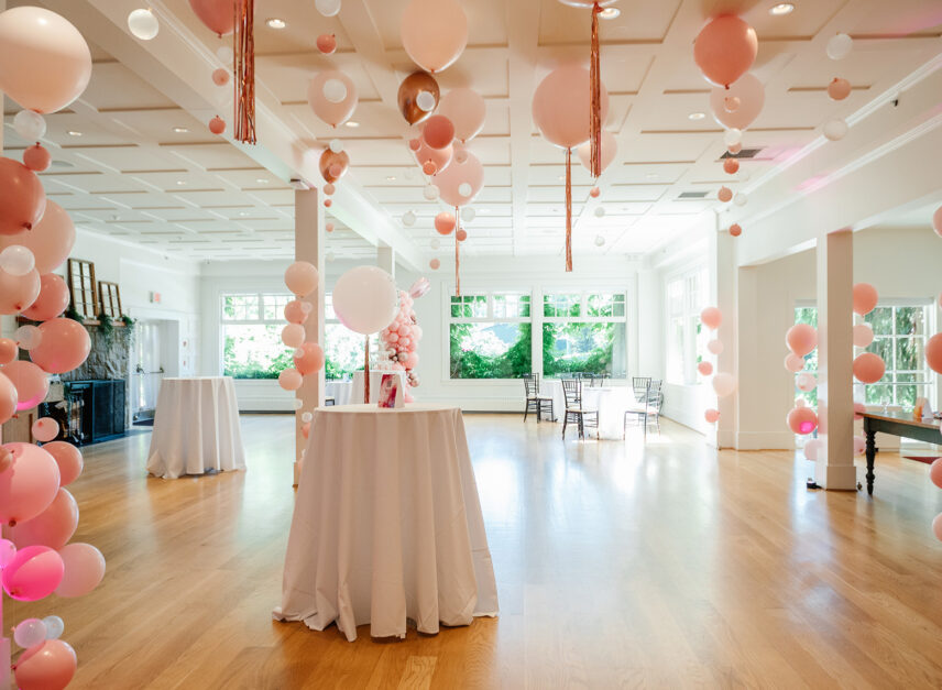 The inside of the Tea Room, set up for a corporate event. Pink balloons decorate the walls and ceilings. Standing tables are draped with white linen.